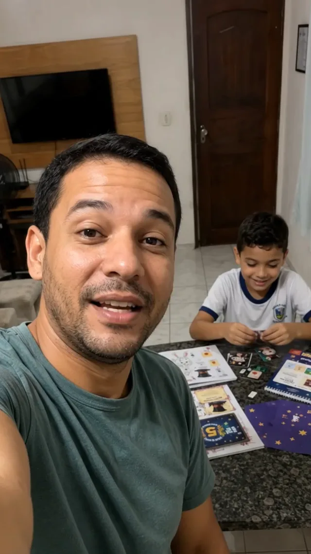 Pai sorrindo com o filho ao fundo brincando com as cartas do kit